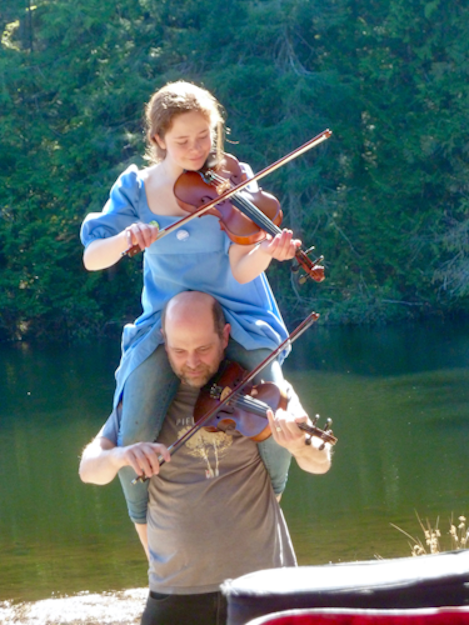 child on dad's shoulders, both playing the fiddle